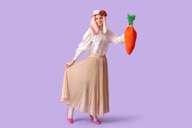 Tavşan kulaklı güzel bir kadın ve leylak arka planda oyuncak havuç tutan şık bir etek. Paskalya kutlaması