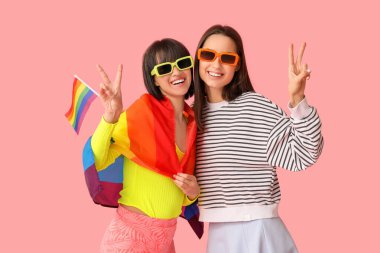 LGBT bayraklı genç lezbiyen çift pembe arka planda zafer jesti gösteriyor