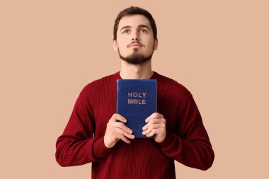 Kahverengi arka planda İncil 'i olan dindar genç bir adam.