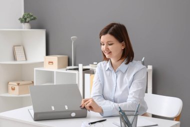 Genç iş kadını modern ofiste masada oturuyor ve klasörü tutuyor.