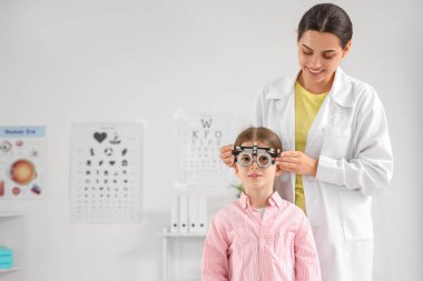 Female ophthalmologist putting trial frame on little girl in clinic