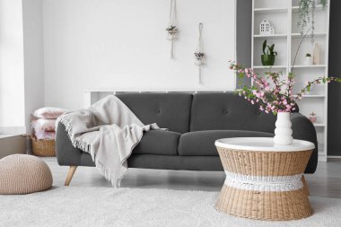 Oturma odasının modern iç mekanı kanepe ve çiçek açan dalları olan kahve masası.