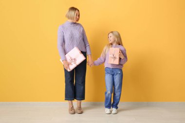 Güzel genç bir kadın ve küçük tatlı kızı sarı duvarın yanında hediye kutuları tutuyor.