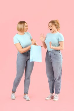 Pembe arka planda alışveriş çantası olan şık kotlu güzel kadınlar.