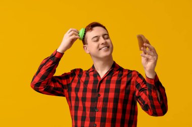 Saç derisi masajcısı ve sarı arka planı olan genç bir adam.