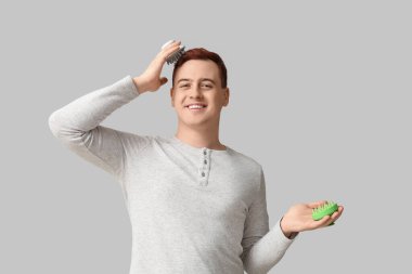 Gri arka planda saç derisi masaj aletleri olan genç bir adam.