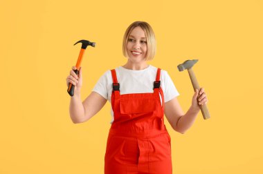 Sarı arka planda çekiçleri olan kadın işçi.