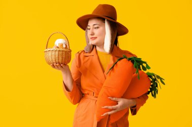 Tavşan kulaklı, oyuncak havuçlu ve sarı arka planda Paskalya sepetli güzel bir genç kadın. Paskalya kutlaması