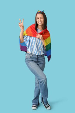 Mavi arka planda zafer jesti gösteren LGBT bayrağıyla güzel genç bir kadın.