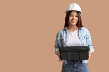 Bej arka planda alet çantası olan genç bir bayan işçi.
