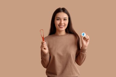 Dil kazıyıcısı ve bej arka planda diş ipi olan genç Asyalı kadın.