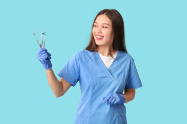 Mavi arka planda diş aletleri olan genç bir dişçi.