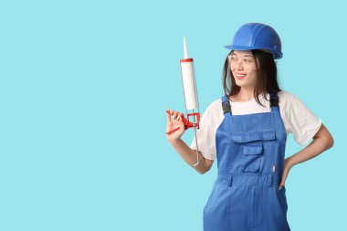 Mavi arka planda kabartma tabancası olan genç bir kadın işçi.