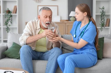Parkinson sendromundan muzdarip yaşlı adam evde hemşireden bir bardak su alıyor.