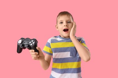 Şok olmuş küçük bir çocuk pembe arka planda joystick ile