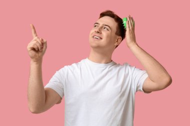 Saç derisi masajcısı kullanan genç bir adam pembe arka plandaki bir şeyi işaret ediyor.