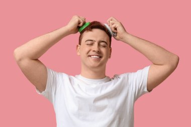 Genç adam pembe arka planda saç derisi masaj aleti kullanıyor.