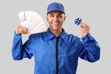 Palet örnekleri ve gri arkaplanda etiket işareti olan yakışıklı erkek ressam.