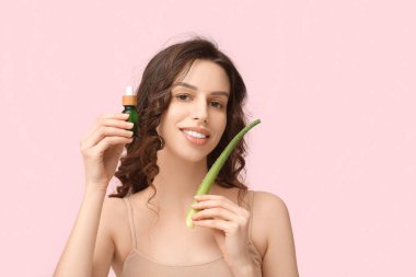 Aloe vera ve pembe arka planda bir şişe serum olan güzel genç bir kadın.