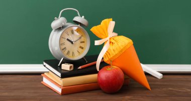 Okul konisi, kitaplar, çalar saat ve elma sınıftaki masada.