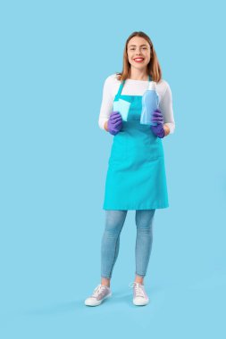 Deterjan şişesi ve mavi arka planda temizlik süngeri olan genç bir kadın.