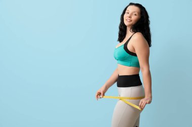 Kalçalarını mavi arka planda ölçen genç ve güzel bir kadın. Kilo verme konsepti