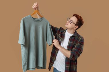 Giysileri bej arka planda olan dolabı açan genç adam.