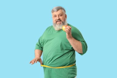 Aşırı kilolu, mutlu, mavi arka planda şerit ve elma olan olgun bir adam. Kilo verme konsepti