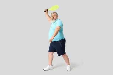 Gri arka planda badminton raketi olan kilolu olgun bir adam. Kilo verme konsepti