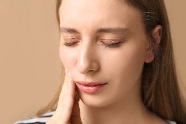 Kahverengi arka planda diş ağrısından muzdarip güzel bir genç kadın. Yakın plan.