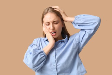 Kahverengi arka planda diş ağrısı çeken genç bir kadın.