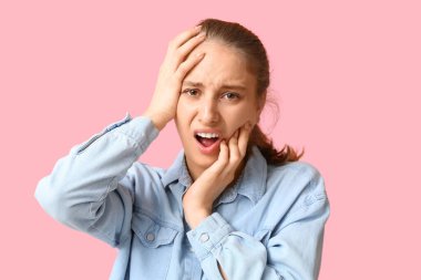 Pembe arka planda diş ağrısı çeken güzel bir genç kadın.