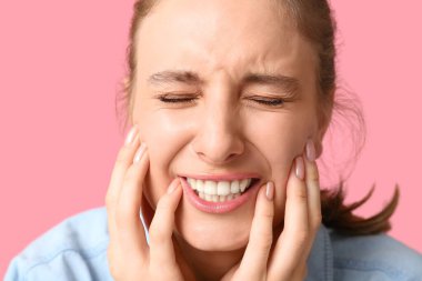 Pembe arka planda diş ağrısından muzdarip güzel genç bir kadın, yakın plan.