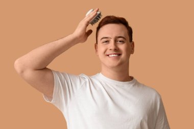 Kahverengi arka planda saç derisi masaj aleti olan genç bir adam.