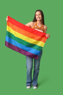 Yeşil arka planda LGBT bayrağı olan mutlu genç bir kadın.