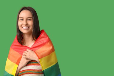 Yeşil arka planda LGBT bayrağı olan mutlu genç bir kadın.