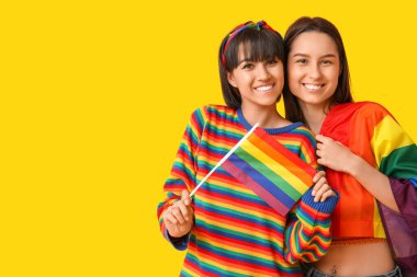 Sarı arka planda LGBT bayrakları olan genç lezbiyen çift
