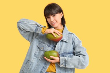 Sarı arka planda olgun mangoları olan güzel genç bir kadın.