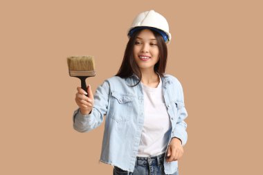 Bej arka planda fırçası olan genç bir kadın ressam.