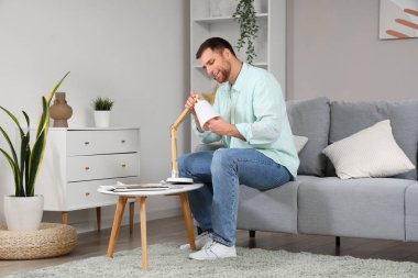 Genç adam oturma odasında masa lambasında ampul değiştiriyor.