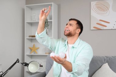 Genç adam evdeki masa lambası için ampul seçiyor.
