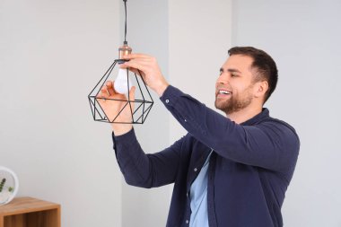 Genç adam evdeki lambada ampul değiştiriyor.