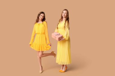 Bej arka planda hediye kutusu olan güzel genç kız kardeşler.