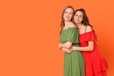 Güzel genç kız kardeşler turuncu arka planda sarılıyorlar.