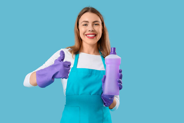 Young woman with bottle of detergent showing thumb-up on blue background