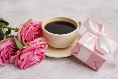 İçinde güzel güller ve beyaz arka planda bir fincan kahve olan hediye kutusu.
