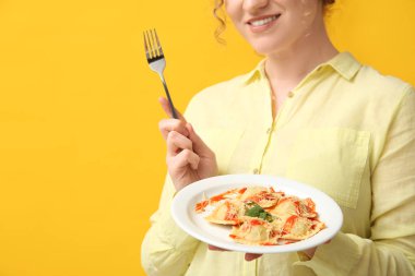 Çatallı ve sarı arka planda lezzetli bir ravioli tabağı olan mutlu genç bir kadın.