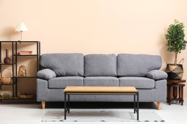 Siyah kanepeli şık bir oturma odası, raf ünitesi ve bej duvarın yanındaki ev bitkileri.