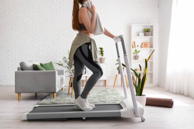 Evde koşu bandında havlu eğitimi alan sportif bir kadın.
