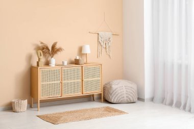 Ahşap çekmeceler, vazo dolusu otlar ve lamba. Odadaki bej duvarın yanında.